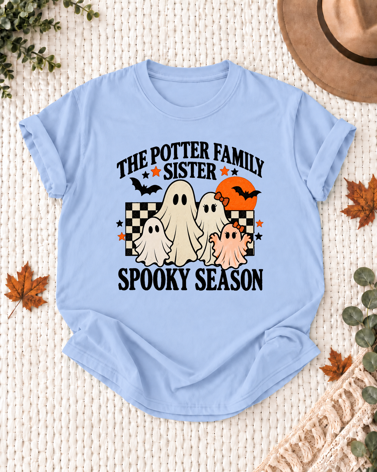 Light blue Sister T-shirt with friendly ghosts, an orange moon, bats, black-and-cream checkerboard accents, and example family-name text.