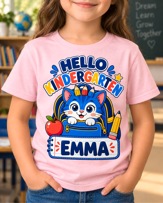 Child wearing a light pink personalized kindergarten backpack cat shirt with the sample name Emma in a classroom.