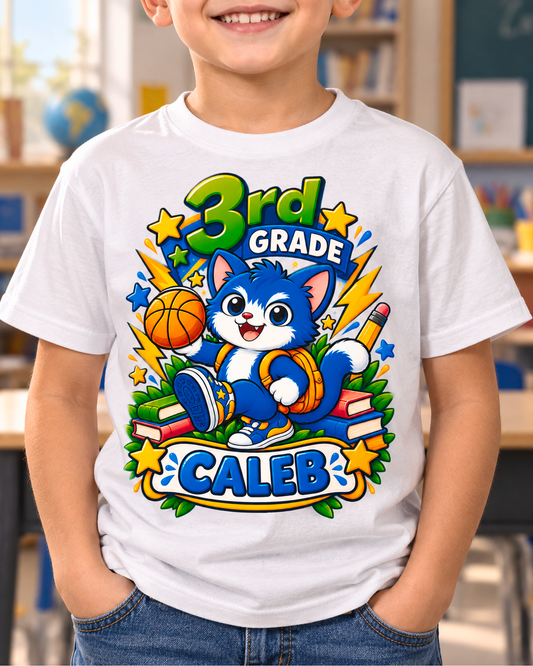 Child wearing a white personalized third grade basketball cat shirt with the sample name Caleb in a classroom.