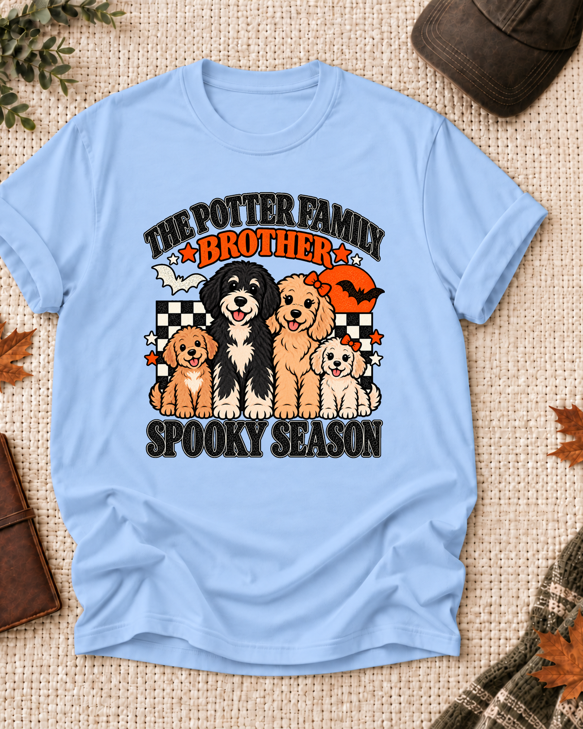 Light blue Brother T-shirt with four illustrated dogs, an orange moon, bats, black-and-cream checkerboard accents, and example family-name text.