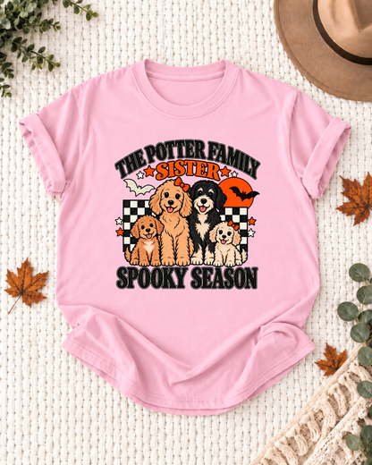 Light pink Sister T-shirt with four illustrated dogs, an orange moon, bats, black-and-cream checkerboard accents, and example family-name text.