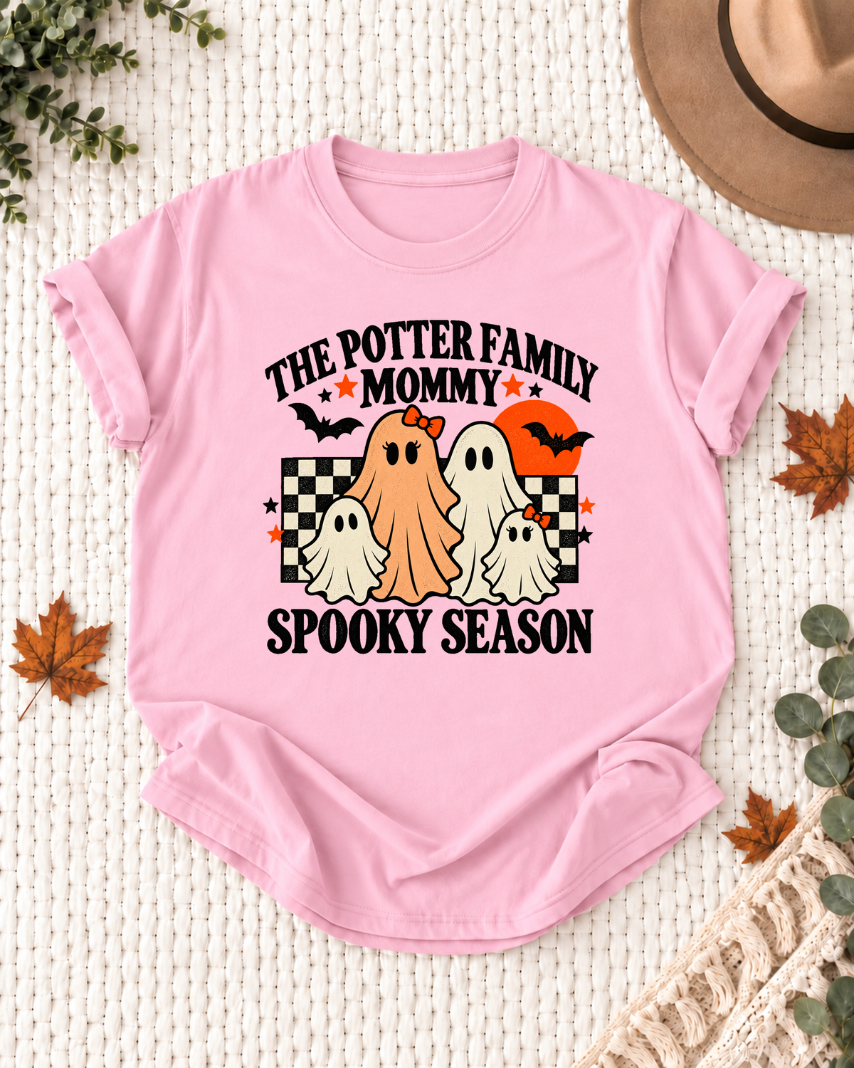 Light pink Mommy T-shirt with friendly ghosts, an orange moon, bats, black-and-cream checkerboard accents, and example family-name text.