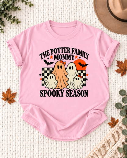 Light pink Mommy T-shirt with friendly ghosts, an orange moon, bats, black-and-cream checkerboard accents, and example family-name text.