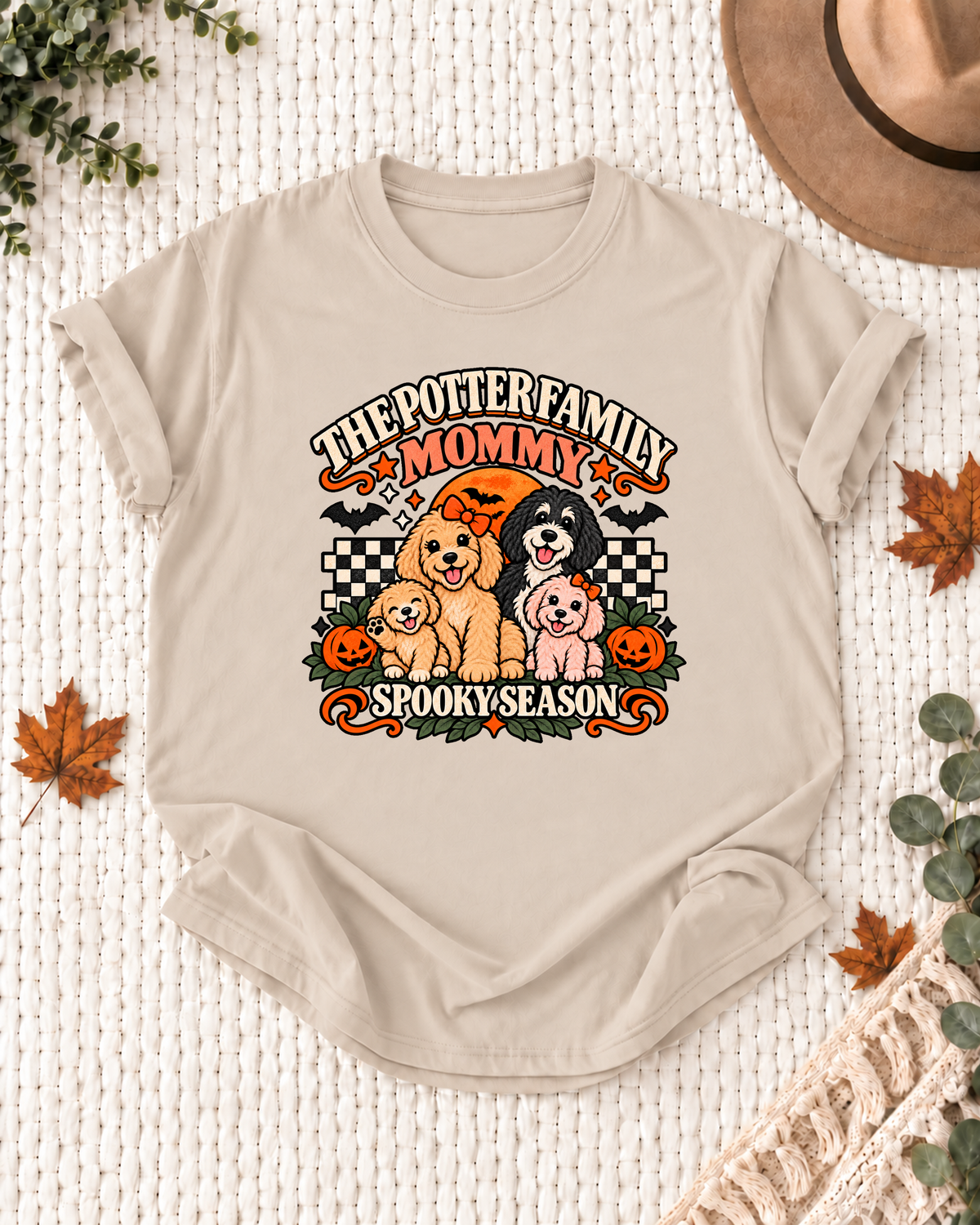 Sand Mommy T-shirt with four dogs, orange bows, jack-o'-lanterns, bats, and checkerboard accents, showing "The Potter Family" as an example and "Spooky Season" below.