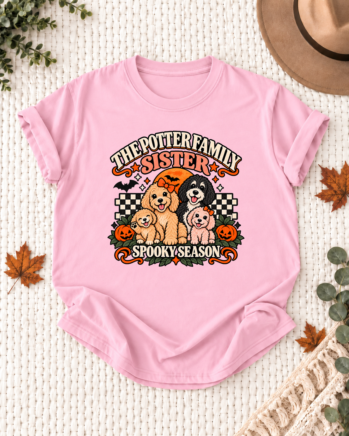 Light pink Sister T-shirt with coral role lettering, four dogs, orange bows, pumpkins, and checkerboard accents, showing the example name "The Potter Family."