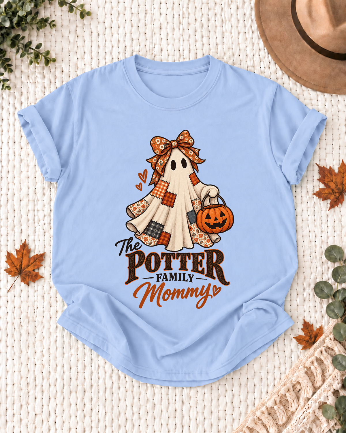 Light blue Mommy T-shirt with a patchwork ghost wearing a bow and scarf, holding a jack-o'-lantern, with example family-name text.