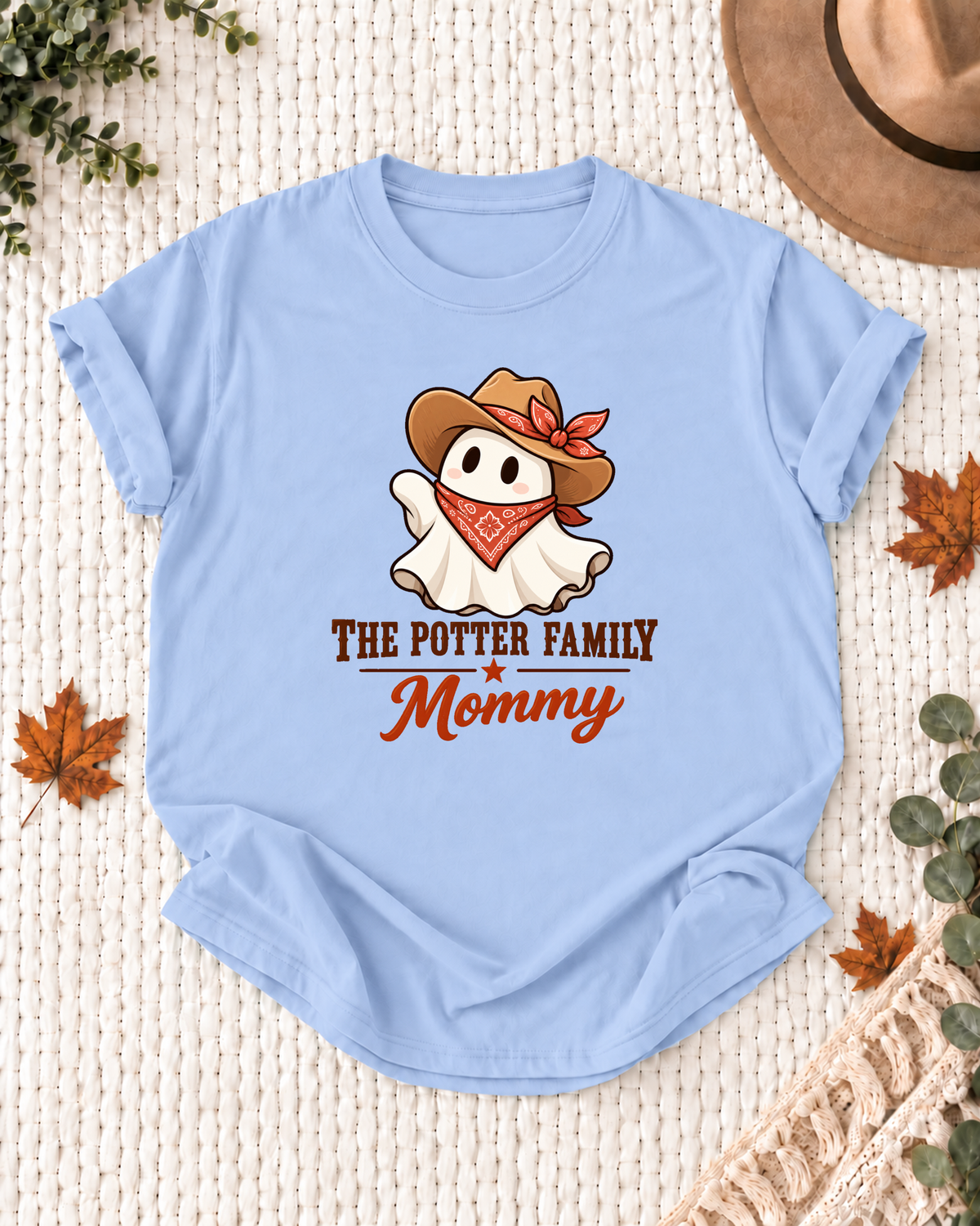 Mommy's Light Blue personalized Halloween shirt mockup with a ghost with a brown cowboy hat, red bandana, and floral bow, sample family lettering, and the role label.